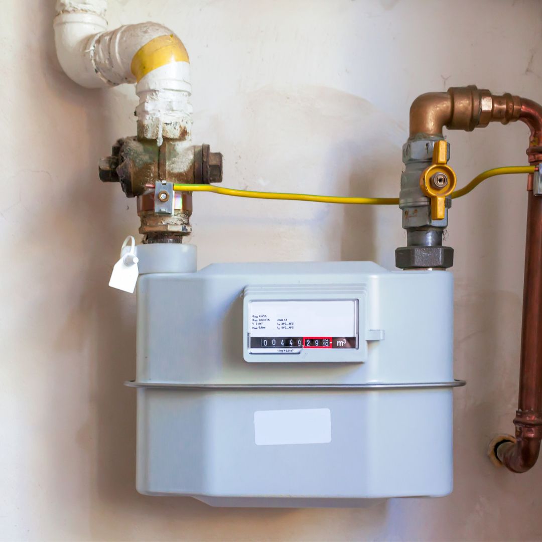 A gas meter with attached pipes and a yellow grounding wire is mounted on a wall, displaying a numerical reading on its digital screen—an essential part of any heating installation.