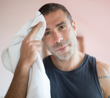 A man in a sleeveless shirt wipes sweat from his forehead with a white towel, looking directly at the camera—perhaps wondering, What Causes AC to Stop Cooling in Irvine?.