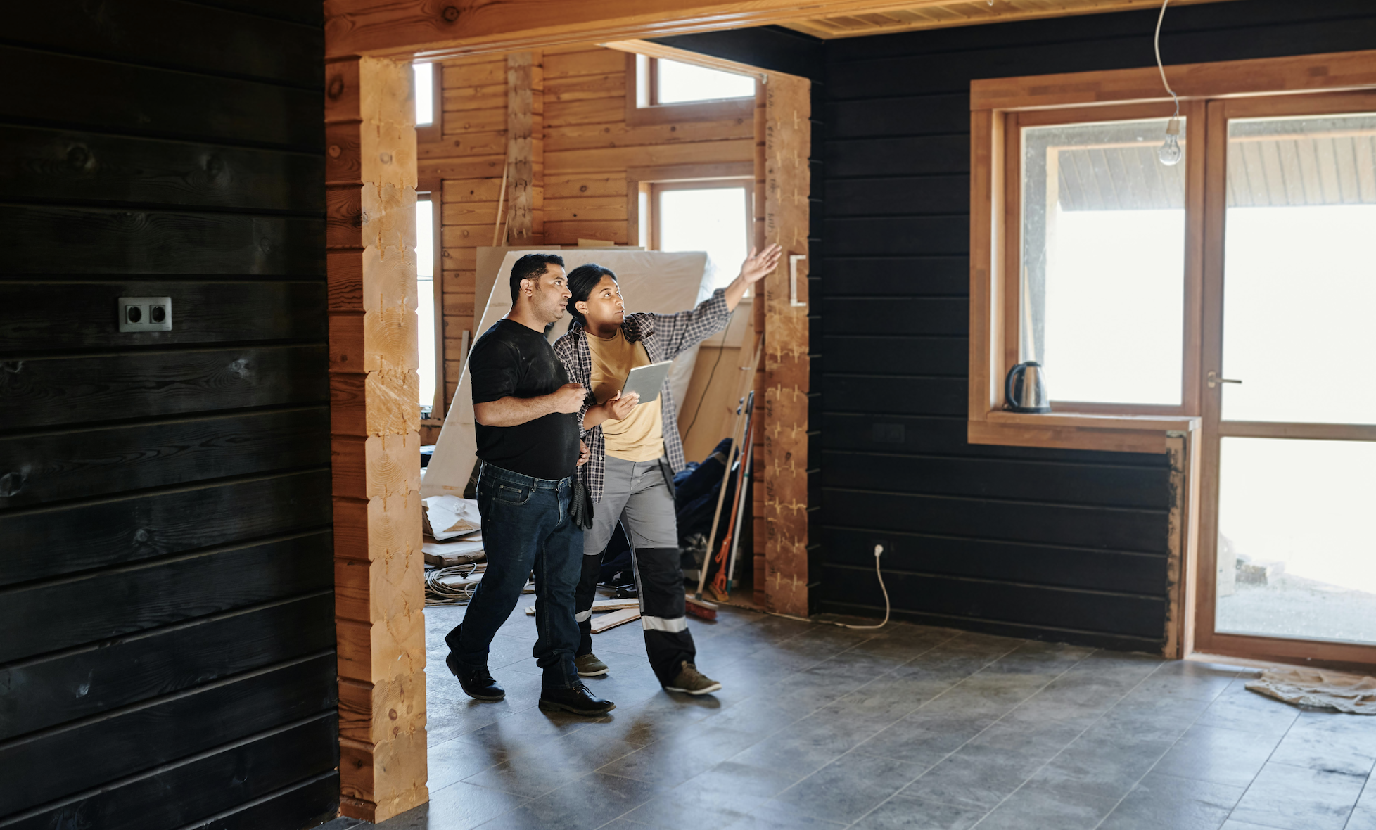 Two people stand in a partially finished wooden interior in Irvine, one gesturing toward the ceiling while discussing construction and asking, "How often should air ducts be inspected in Irvine, CA?.
