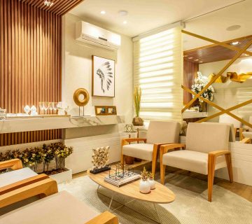 Modern waiting room with beige chairs, a coffee table, decorative wall art, flowers, and a mirrored wall with gold accents. Warm lighting and wood paneling create a cozy atmosphere—perfect for discussing what are the benefits of upgrading to a new AC unit in Irvine.