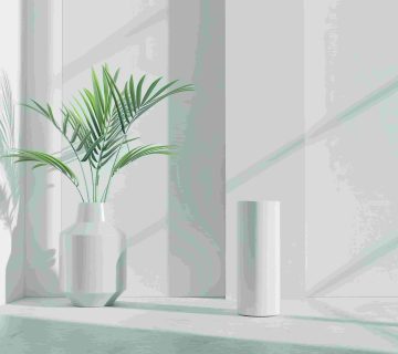 A green potted plant in a white vase sits next to a tall white cylindrical dehumidifier in a sunlit minimalist room, subtly echoing the debate: Dehumidifier vs  AC—which cools better in OC? Shadows dance across the wall, enhancing the serene ambiance 