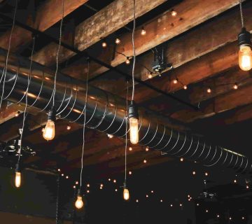 Exposed ceiling with wooden beams, metal ductwork, and hanging Edison style light bulbs create a warm, industrial atmosphere—ideal for discussing topics like “What Are the Common Problems with Air Ducts in Irvine Homes?” 