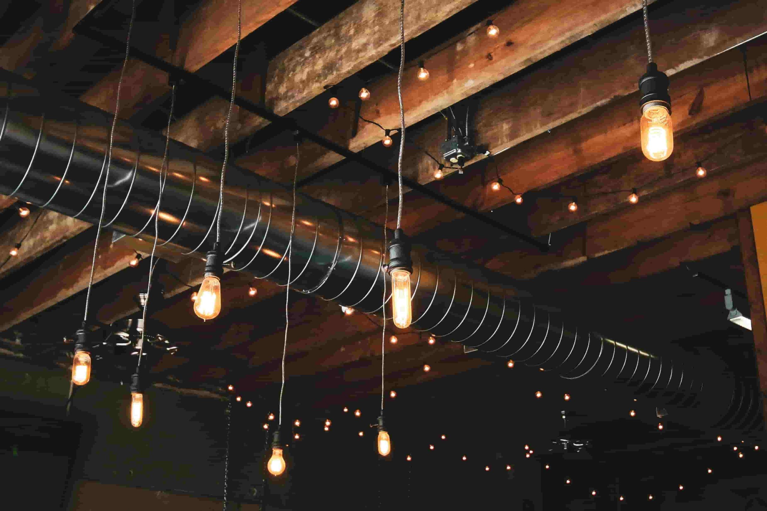 Exposed ceiling with wooden beams, metal ductwork, and hanging Edison style light bulbs create a warm, industrial atmosphere—ideal for discussing topics like “What Are the Common Problems with Air Ducts in Irvine Homes?” 